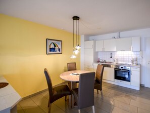 Eine moderne Küche mit weißen Schränken, einem eingebauten Backofen und einer Essecke mit rundem Tisch und Stühlen.
