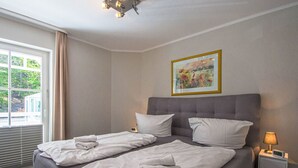 Una camera d'albergo con un letto, un comodino con una lampada, un quadro appeso al muro e una finestra con tende.