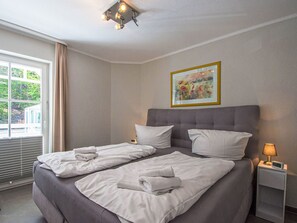 Ein Hotelzimmer mit einem Bett, einem Nachttisch mit Lampe, einem Bild an der Wand und einem Fenster mit Vorhängen.