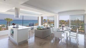 A modern living room with a large window overlooking the sea, a dining area with a glass table, and a kitchen with a central island. - Luxuriöse Wohnung am Strand von Thalassa by Interhome (Paralimni)