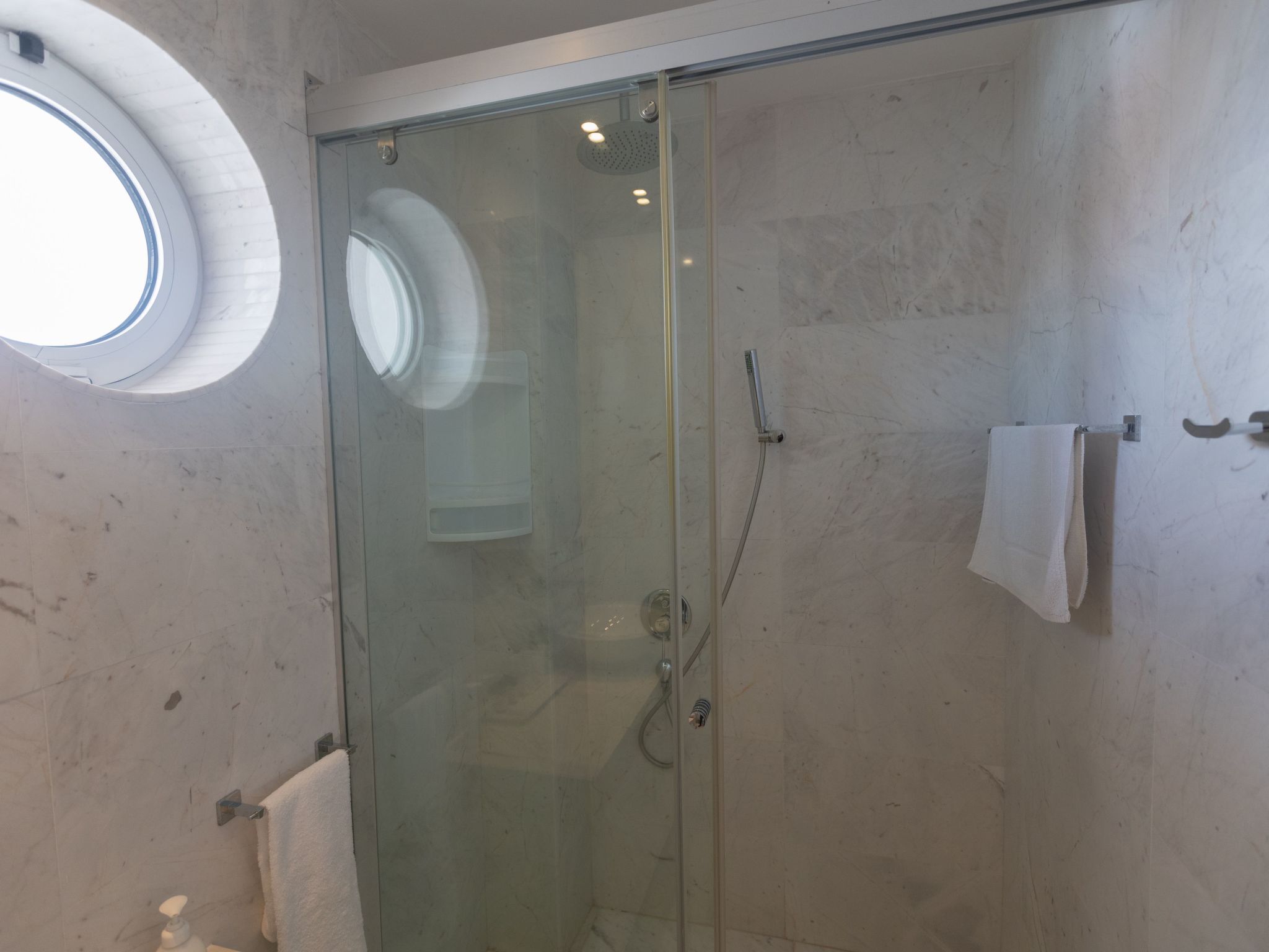 A glass-enclosed shower with a handheld showerhead, a towel rack with a towel, and a soap dispenser on the wall.
