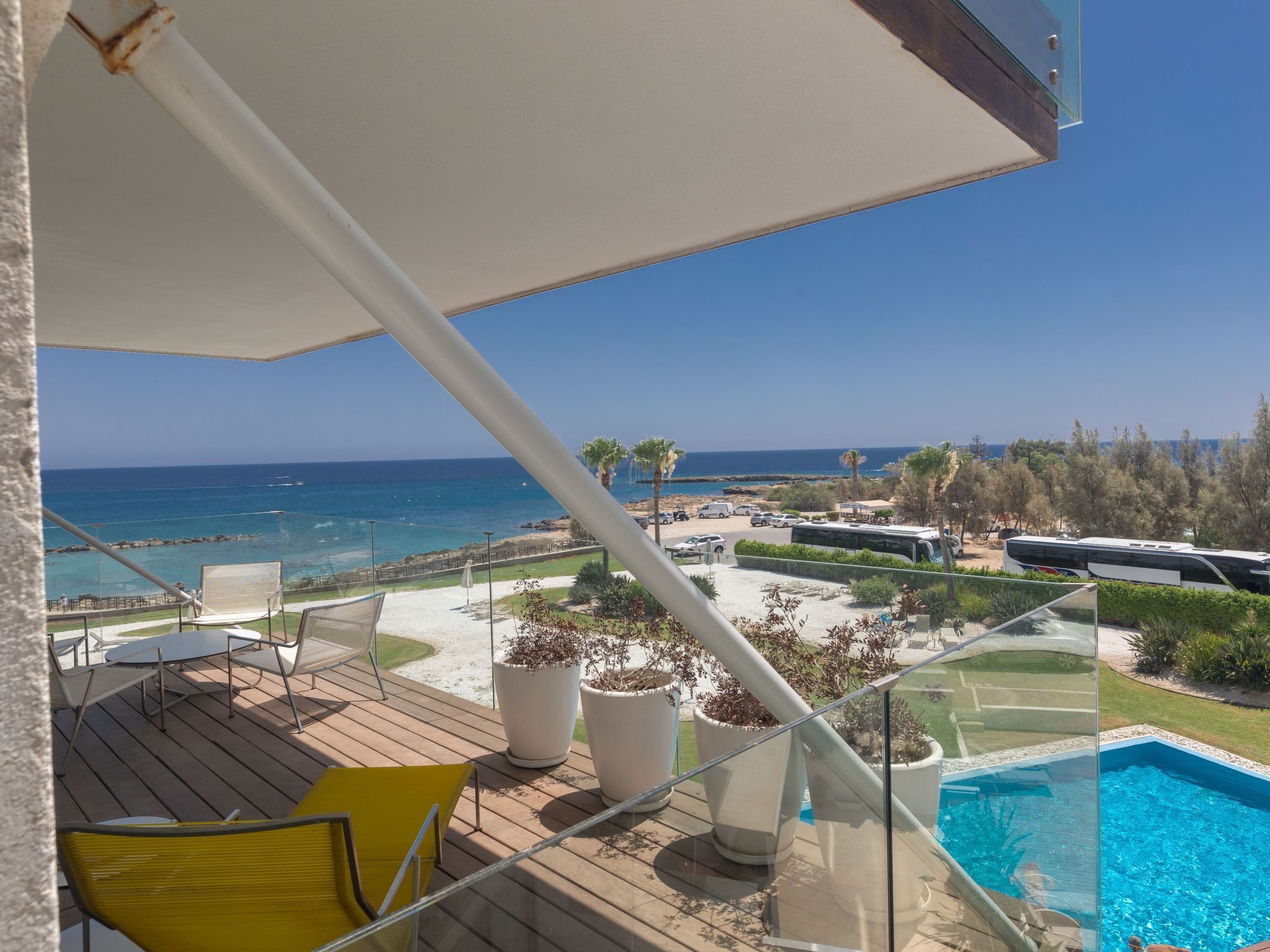 En balkon med pool, udendørs møbler og udsigt til hav og strand.