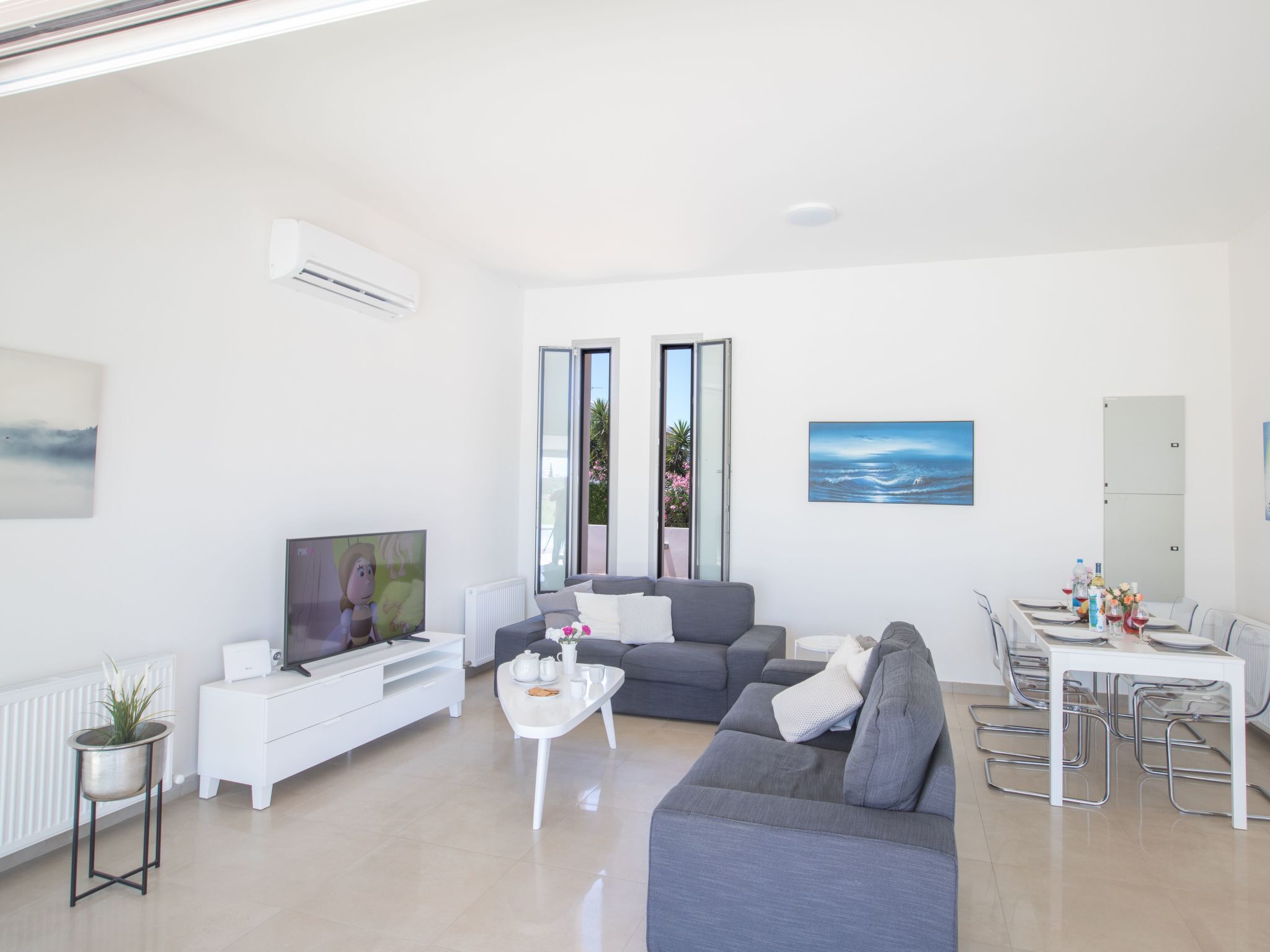 A modern living room with a grey sofa, a coffee table, a TV, and a dining area with a table set for two. - in Ayia Napa mit großem Patio by Interhome (Ayia Napa)