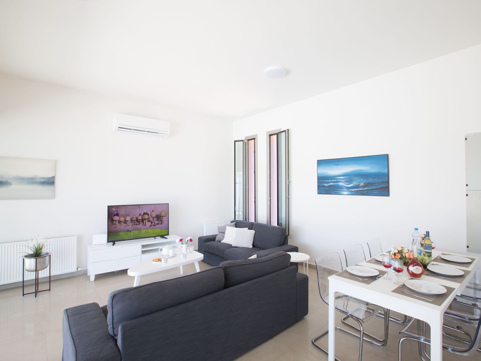 A modern living room with a grey sofa, a white coffee table, and a dining table set for four.
