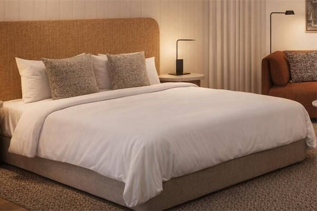 Een netjes opgemaakt bed met witte lakens, twee nachtkastjes met lampen, en een bruine gestoffeerde fauteuil.