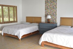 A bedroom with two wooden beds, a nightstand with a lamp, and a floral wallpaper on the wall. - Hooked on Panama Hotel (Limones)