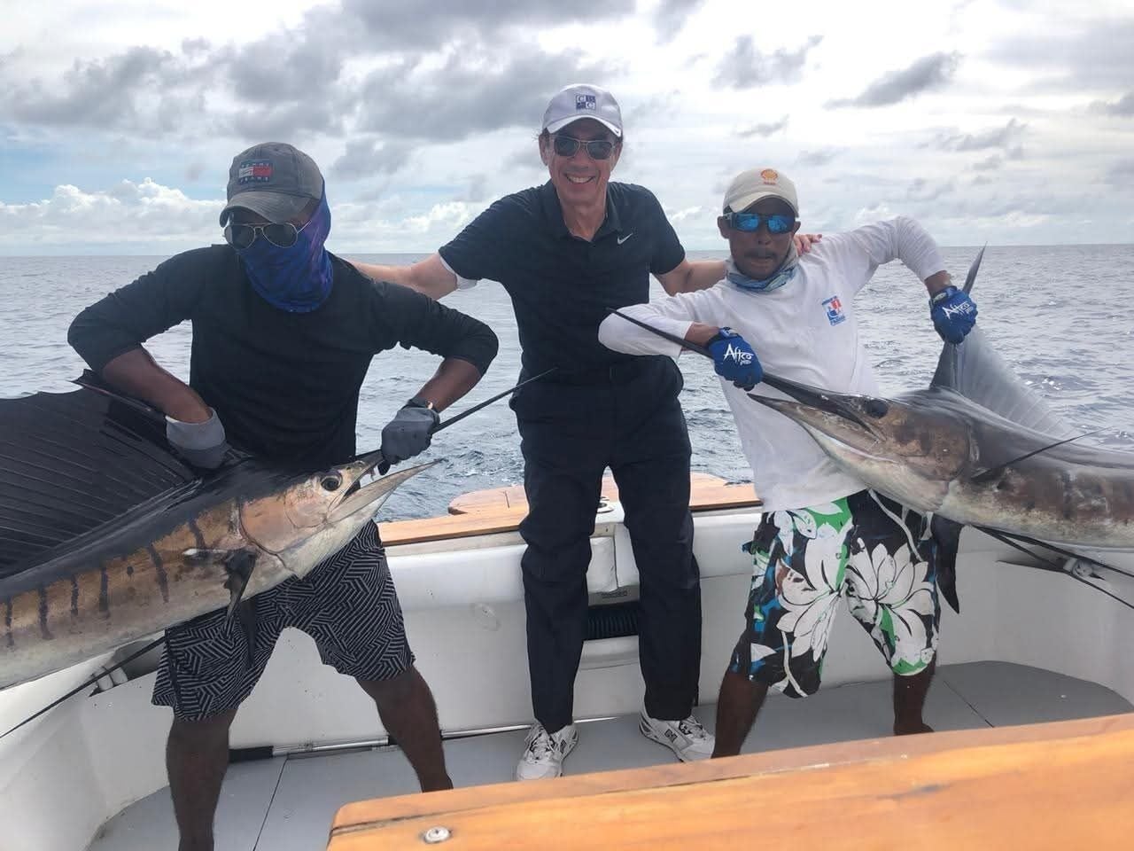 Three people on a boat holding large fish.