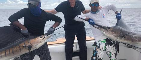 Three people on a boat holding large fish.