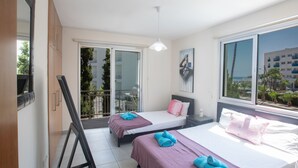 Camera d'albergo con due letti, un balcone e una grande finestra che si affaccia su edifici e alberi.