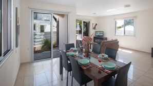 Zona pranzo con tavolo apparecchiato per quattro persone, una televisione sullo sfondo e una porta vetrata scorrevole che dà su un'area esterna.