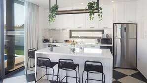 Una cocina moderna con armarios blancos, un refrigerador de acero inoxidable, una cafetera y plantas colgantes.