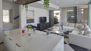 Una sala de estar moderna con un sofá, una mesa de centro y un televisor. Hay una zona de cocina con armarios y una encimera.