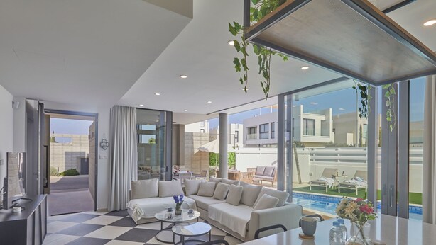 Una sala de estar moderna con piso a cuadros, un conjunto de sofá, una mesa de centro y vistas a una piscina y edificios exteriores.