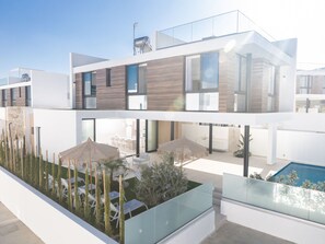 Ein modernes, zweistöckiges Haus mit flachem Dach, großen Fenstern und einem Swimmingpool.