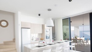 A modern kitchen with a central island, white bar stools, and a dining area with a table and chairs. - Protaras Aqua Pearl Villa AQ16 by Interhome (Protaras)
