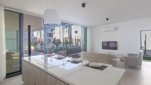 A modern kitchen with a large island, a dining area with a glass table, and a living room with a sofa and TV. - Protaras Aqua Pearl Villa AQ16 by Interhome (Protaras)