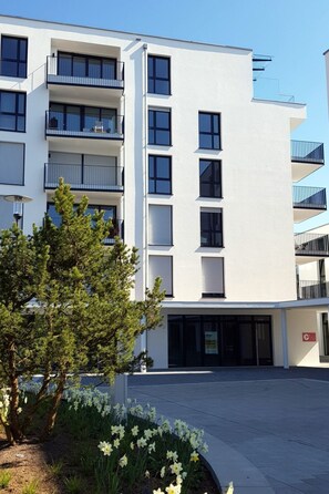 A modern multi-story building with balconies, a parking area, and a garden with daffodils. - Pfänder by Interhome (Friedrichshafen)