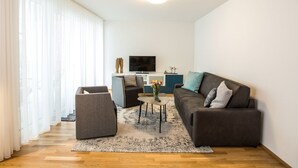 A modern living room with a sofa, armchair, and coffee table, a flat-screen TV, and a decorative vase with flowers. - Pfänder by Interhome (Friedrichshafen)