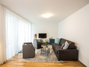 A modern living room with a sofa, armchair, and coffee table, a flat-screen TV, and a decorative vase with flowers. - Pfänder by Interhome (Friedrichshafen)