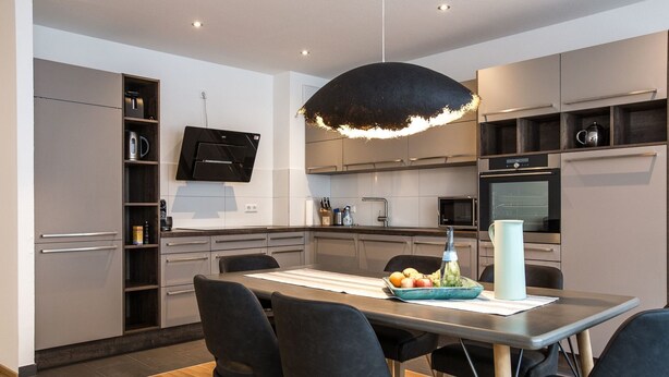 A modern kitchen with a dining area, featuring a large table, four chairs, a TV mounted on the wall, and various kitchen appliances. - Pfänder by Interhome (Friedrichshafen)