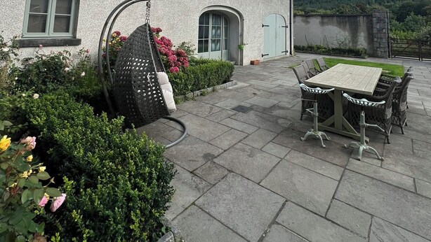 Rakennuksessa on patio, jossa on riipputuoli, pöytä ja tuolit sekä puutarha, jossa kasvaa monenlaisia kasveja ja kukkia.