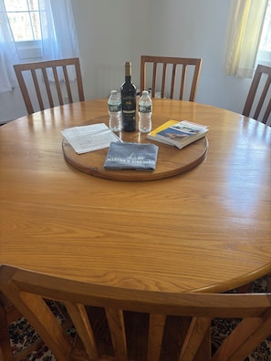 A round wooden table with a placemat, two bottles of water, a bottle of wine, a book, and a t-shirt on it.