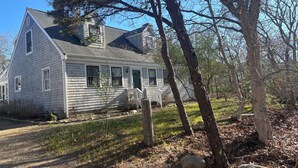 A two-story house with a front porch, surrounded by trees and a gravel driveway.