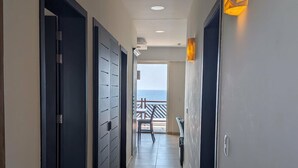Een gang met donkere deuren, ingebouwde verlichting en uitzicht op zee door een open deur aan het einde.