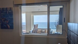 Een slaapkamer met een groot raam met uitzicht op zee, een bed met witte beddengoed en een schilderij aan de muur.