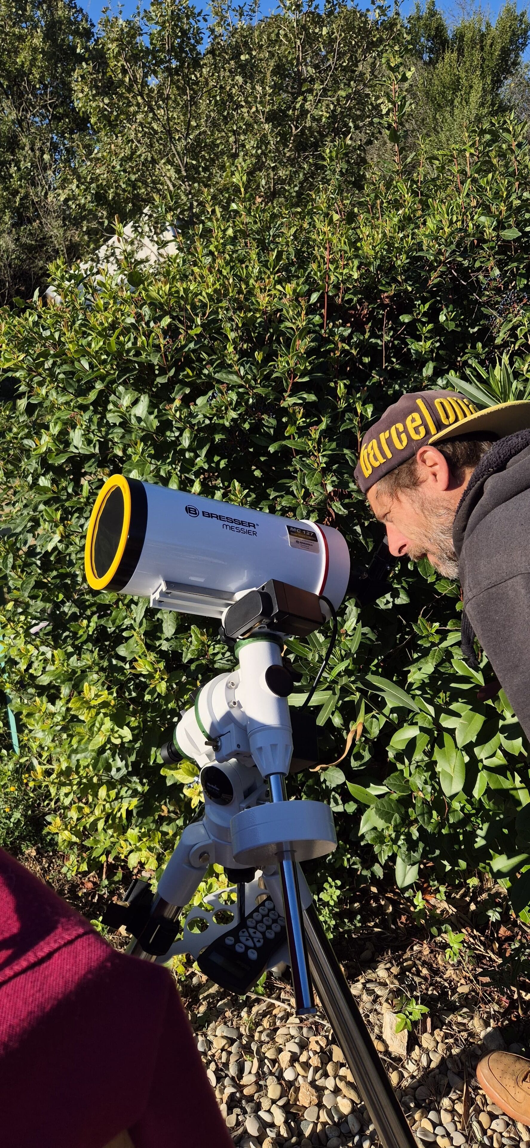 Un télescope doté d’un anneau jaune, installé à l’extérieur, avec un feuillage dense en arrière-plan.