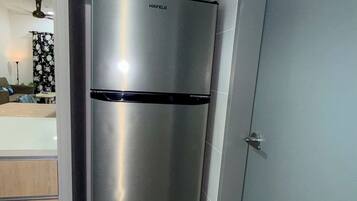 A modern kitchen with a stainless steel refrigerator, a grey door, and a tiled floor.