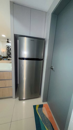A modern kitchen with a stainless steel refrigerator, a grey door, and a tiled floor.