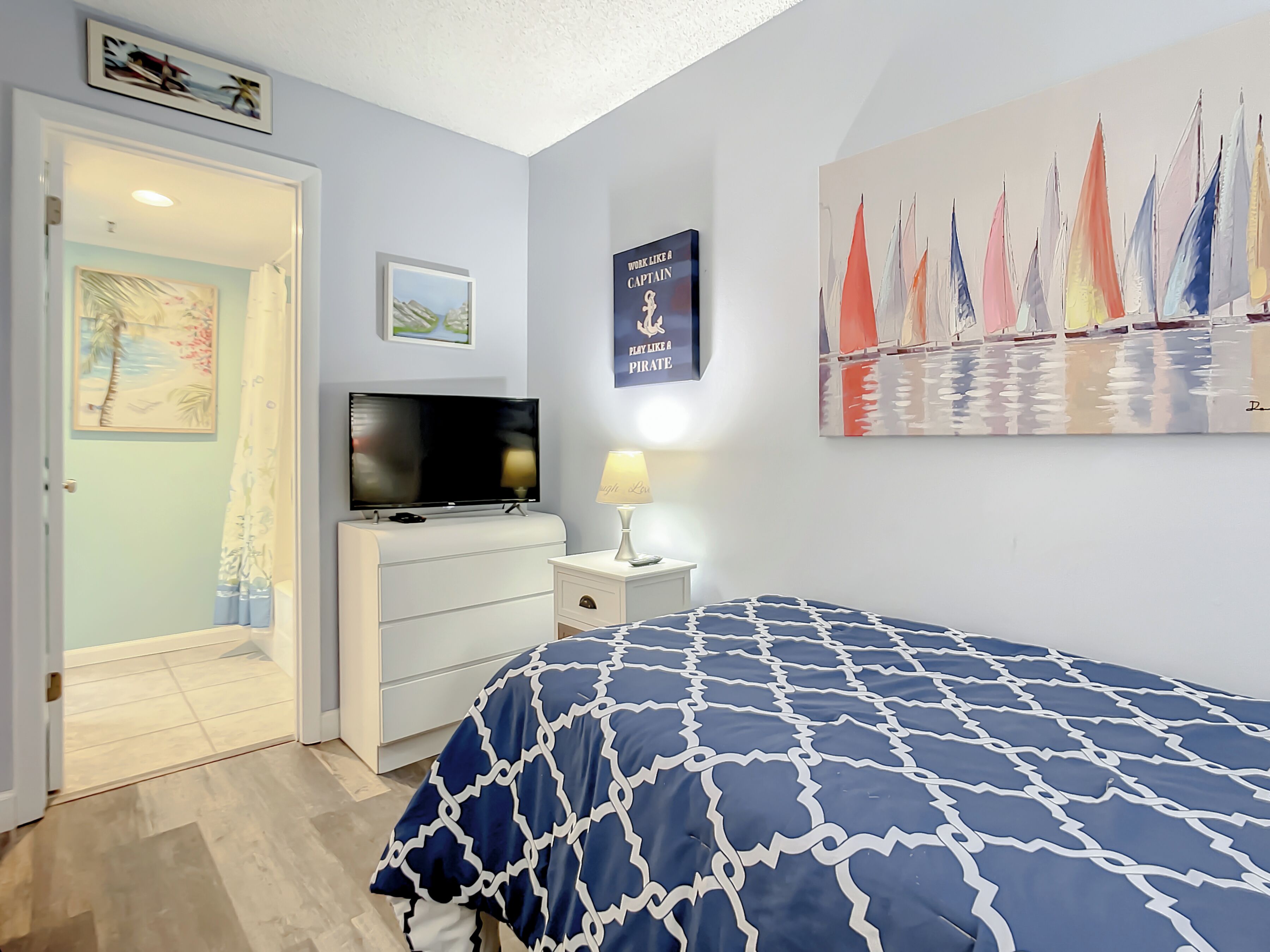 A bedroom with a bed, a TV, a dresser, and a painting of sailboats.
