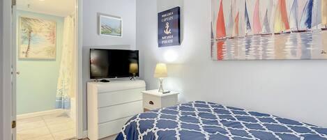 A bedroom with a bed, a TV, a dresser, and a painting of sailboats.