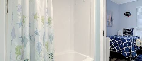 A bathroom with a bathtub, a shower curtain with sea creature patterns, and a bed with a nautical-themed bedspread.