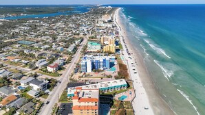 An aerial view of a coastal town with a beachfront, residential buildings, and a hotel with a pool. - Oceania Beach Club 604 (New Smyrna Beach)