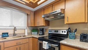 A kitchen with wooden cabinets, a stainless steel stove, a coffee maker, and a toaster. - Oceania Beach Club 604 (New Smyrna Beach)