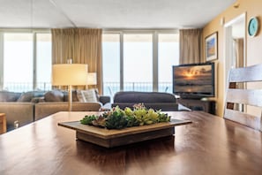 A wooden coffee table with a succulent arrangement in a modern living room with a sofa, a lamp, and a television. - Oceania Beach Club 604 (New Smyrna Beach)