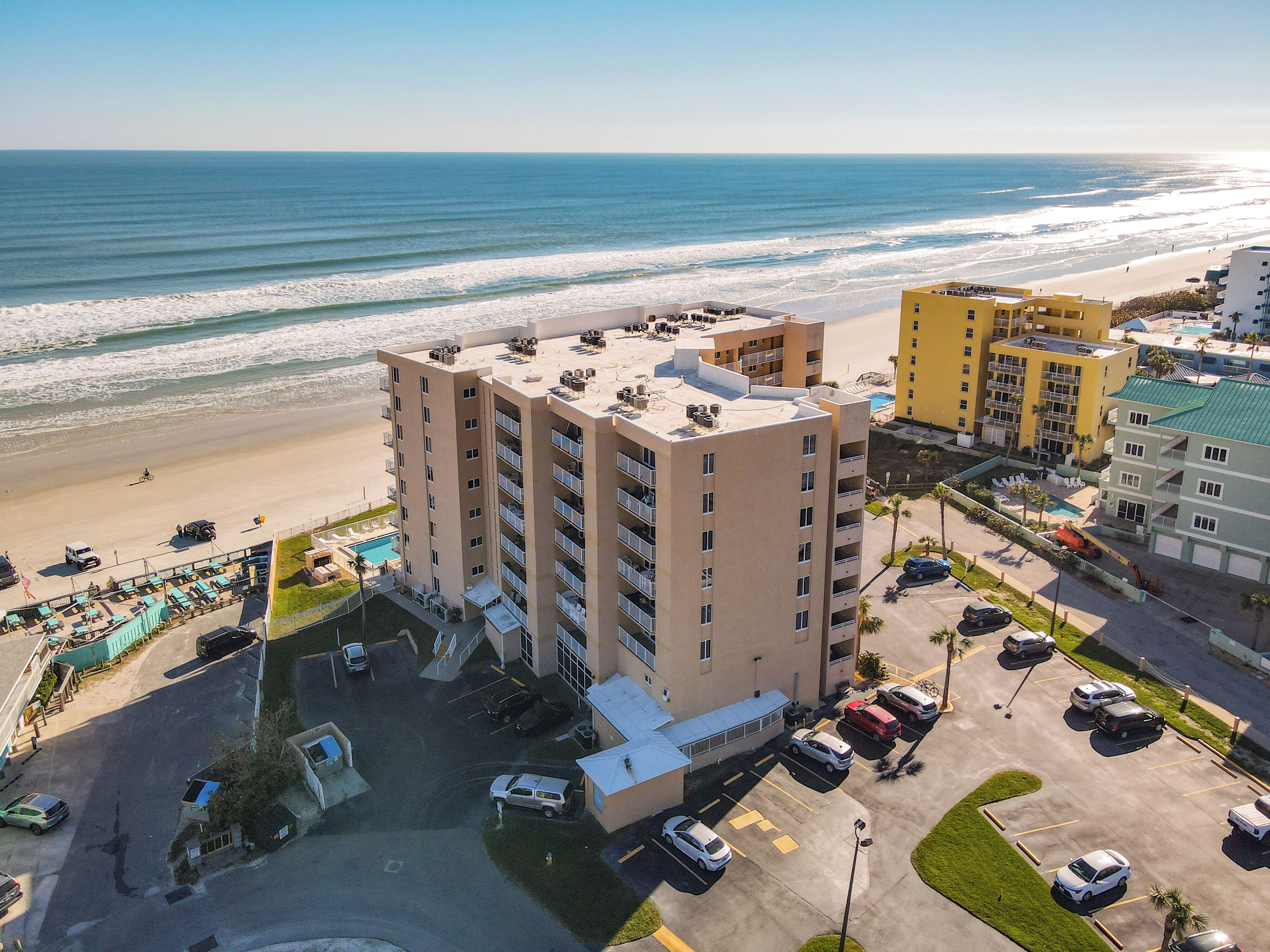 A beachfront hotel with multiple floors, a parking lot, and a view of the ocean.