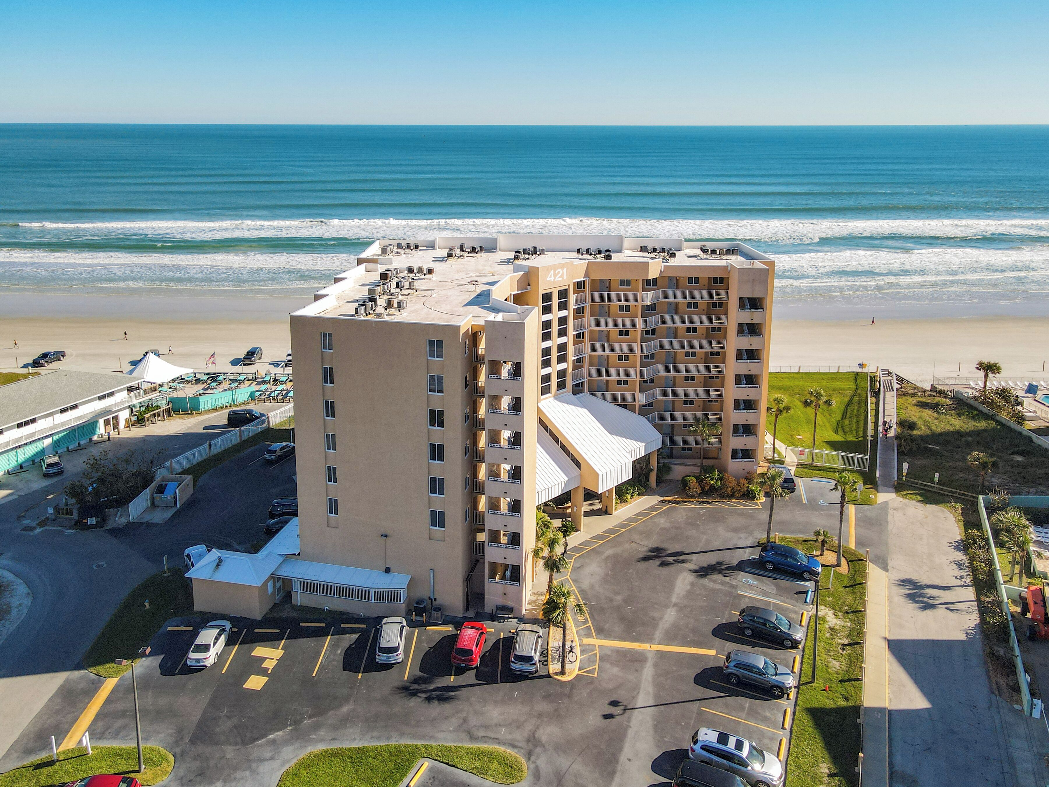 Un hotel de varios pisos con vista a la playa, estacionamiento y zona de piscina.