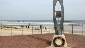 Ein Weg direkt am Strand, mit einer modernen Skulptur und Blick aufs Meer.