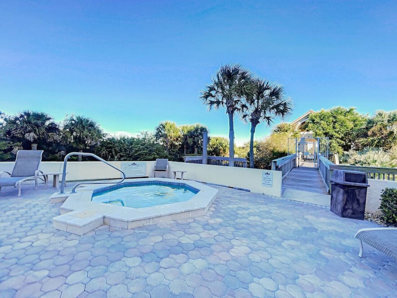 A swimming pool with a hot tub, surrounded by hexagonal tiles, and a bridge leading to a building.
