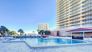 A swimming pool with hexagonal tiles, surrounded by lounge chairs and a covered seating area. - New Smyrna Beachfront Modern 9th Floor Condo Pool Hot Tub (New Smyrna Beach)