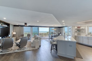 A modern living room with a large TV, seating, and a view of the ocean. - New Smyrna Luxury Beachfront Condo Pool Hot Tub (New Smyrna Beach)