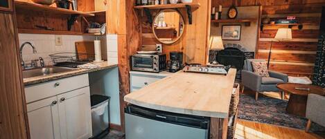 A compact kitchen with a dishwasher, microwave, and coffee maker, wooden cabinets, and a dining area with a sofa and table.
