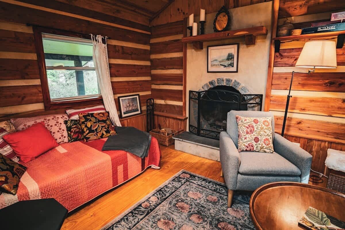 L’intérieur d’un chalet accueillant, avec une cheminée, un canapé, un fauteuil et un plancher en bois.