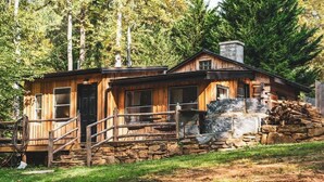 A rustic cabin with a stone foundation, wooden exterior, and a porch with a railing. - Hawthorne Cabin ~ NEW ~ Romantic ~ Unique ~ Serene (Nellysford)