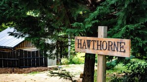 A wooden sign with the name 'HAWTHORNE' in a rustic setting with a building and trees in the background. - Hawthorne Cabin ~ NEW ~ Romantic ~ Unique ~ Serene (Nellysford)