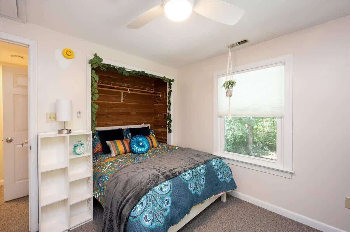 A bedroom with a bed, a ceiling fan, a window with a view, and a white door.