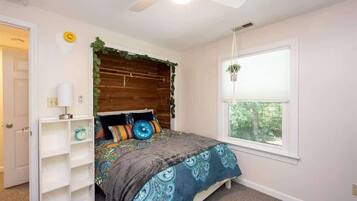 A bedroom with a bed, a ceiling fan, a window with a view, and a white door.